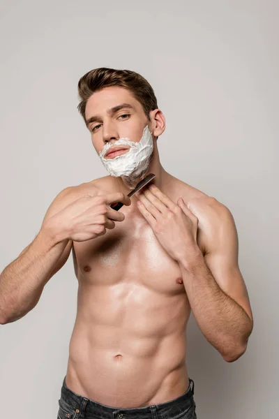 Sexy man with muscular torso shaving with straight razor isolated on grey — Stock Photo