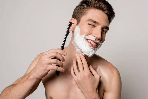 Smiling sexy man with muscular torso shaving with straight razor isolated on grey — Stock Photo