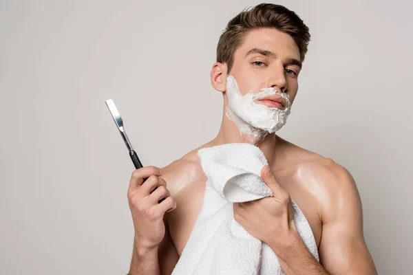 Sexy man with muscular torso and shaving foam on face holding straight razor and towel isolated on grey — Stock Photo