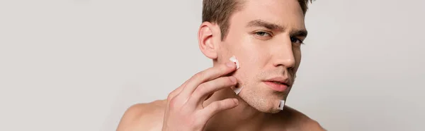 Sexy man with muscular torso touching bloody wounds after shaving on face isolated on grey, panoramic shot — Stock Photo