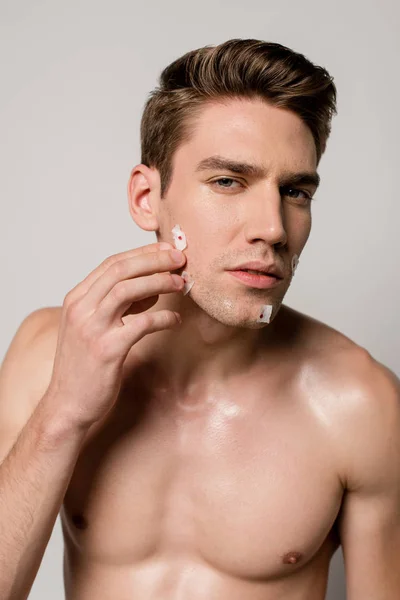 Sexy man with muscular torso touching bloody wounds after shaving on face isolated on grey — Stock Photo