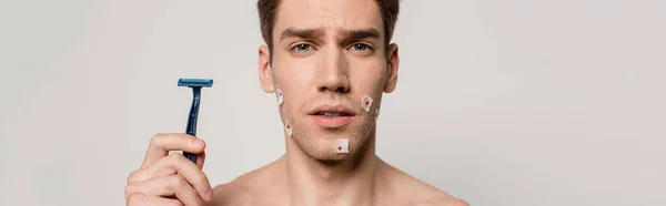 Uomo sexy con busto muscolare e ferite sanguinanti dopo la rasatura tenuta rasoio isolato su grigio, colpo panoramico — Foto stock