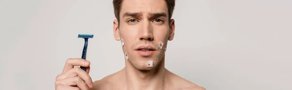 Sexy man with muscular torso and bloody wounds after shaving holding shaver isolated on grey, panoramic shot — Stock Photo