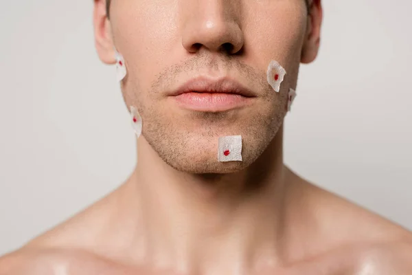 Vista recortada de hombre desnudo con heridas sangrientas después de afeitarse en la cara aislado en gris - foto de stock