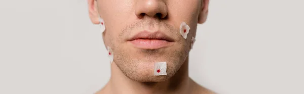 Vista recortada de hombre desnudo con heridas sangrientas después de afeitarse en la cara aislado en gris, tiro panorámico - foto de stock