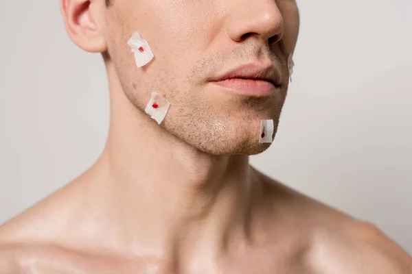 Vista recortada de hombre desnudo con heridas sangrientas después de afeitarse en la cara aislado en gris - foto de stock