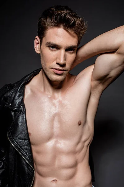 Sexy young man with muscular torso putting on biker jacket on black background — Stock Photo