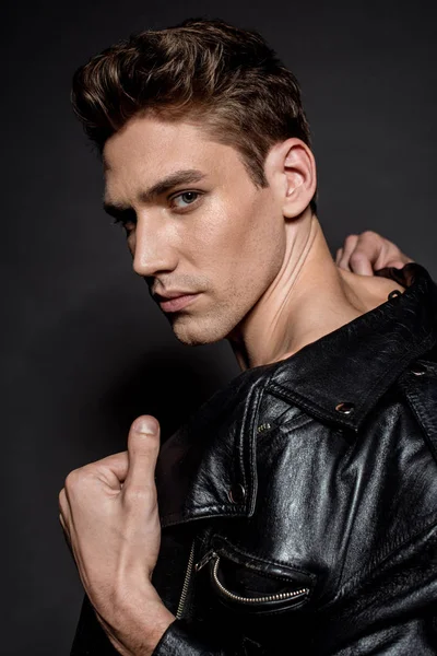 Sexy young man with muscular torso in biker jacket looking at camera on black background — Stock Photo