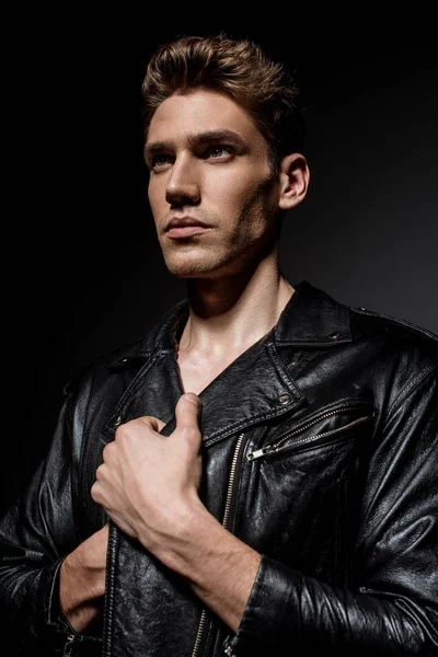 Сексуальный молодой человек в байкерской куртке смотрит в сторону на черном фоне — стоковое фото
