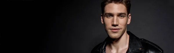 Smiling handsome sexy young man in biker jacket on black background, panoramic shot — Stock Photo
