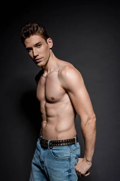 Sexy joven con torso muscular en jeans posando sobre fondo negro - foto de stock