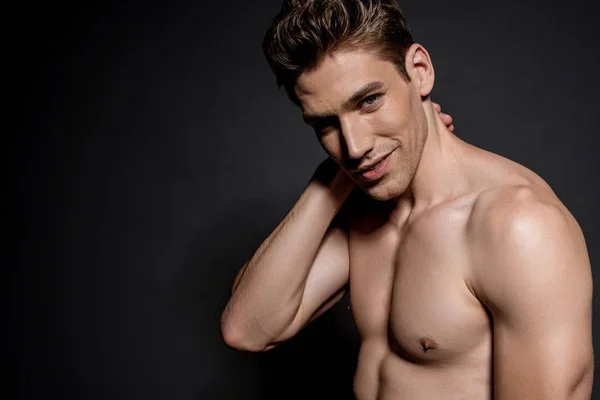 Sonriente sexy joven desnudo hombre con muscular torso posando sobre negro fondo - foto de stock