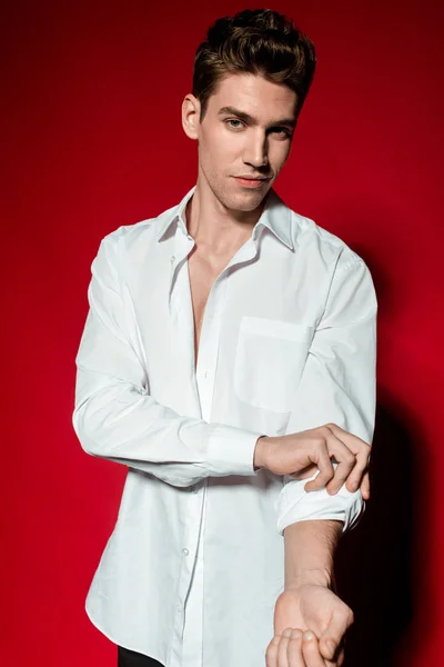 Sexy giovane uomo elegante in camicia sbottonata arrotolando le maniche su sfondo rosso — Foto stock