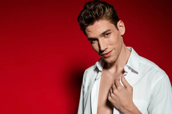 Sexy jeune homme élégant en chemise déboutonnée sur fond rouge — Photo de stock