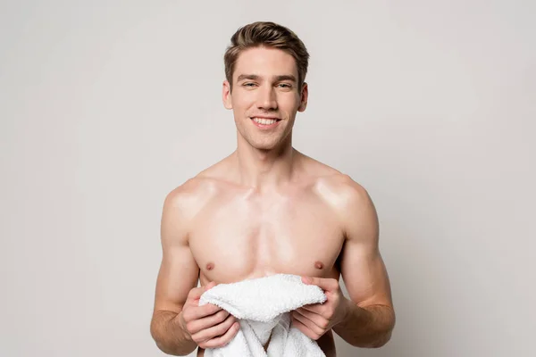 Smiling sexy young naked man holding cotton towel isolated on grey — Stock Photo