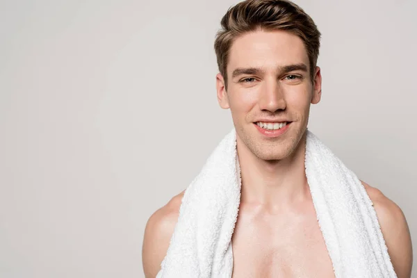 Улыбающийся сексуальный молодой голый мужчина с хлопковым полотенцем, изолированным на сером — стоковое фото