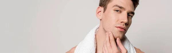 Smiling sexy young naked man with cotton towel touching face isolated on grey, panoramic shot — Stock Photo