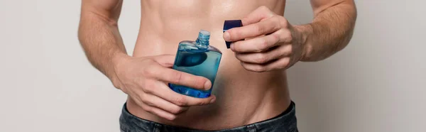 Ausgeschnittene Ansicht eines sexy Mannes mit muskulösem Oberkörper mit After Shave Lotion isoliert auf grauem, panoramischem Foto — Stockfoto