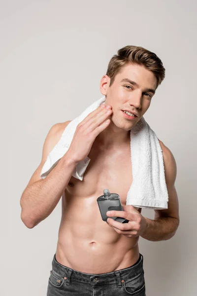 Sexy man with muscular torso with after shave lotion and towel touching face isolated on grey — Stock Photo