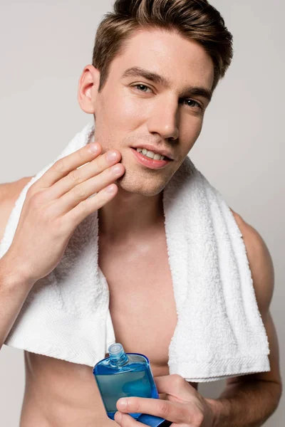 Sexy uomo con busto muscolare con dopobarba lozione e asciugamano toccare il viso isolato su grigio — Foto stock