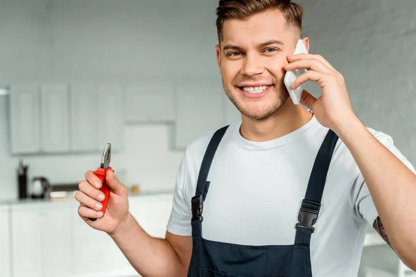 Glücklicher Installateur spricht mit Smartphone und hält Zange — Stockfoto