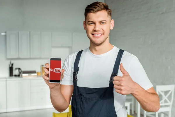KYIV, UKRAINE - DECEMBER 4, 2019: happy installer holding smartphone with youtube app on screen and showing thumb up — Stock Photo