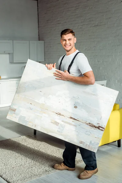Cheerful installer holding painting while standing near carpet — Stock Photo
