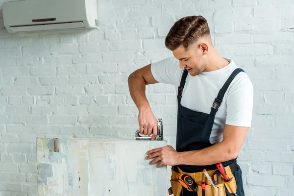 Fröhlicher Installateur hält Bauklammer in der Nähe der Malerei — Stockfoto