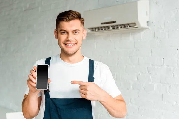 Cheerful installer pointing with finger at smartphone with blank screen — Stock Photo