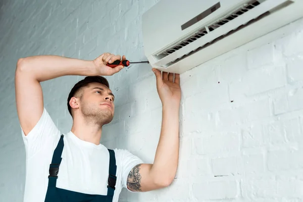 Handsome tattooed installer holding screwdriver near air conditioner — Stock Photo