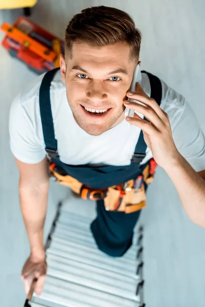 Top view of happy installer climbing ladder and talking on smartphone — Stock Photo