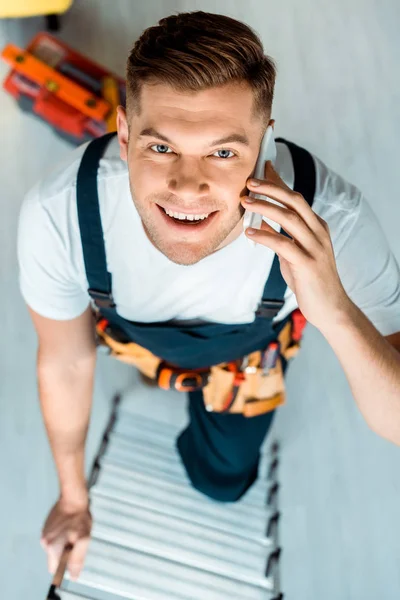 Top view of happy installer climbing ladder and talking on smartphone — Stock Photo