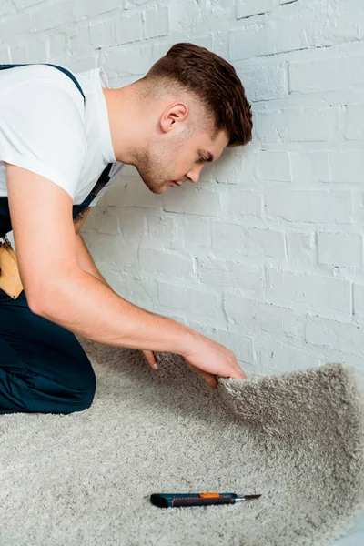 Side view of handsome installer holding carpet near cutter and brick wall — Stock Photo