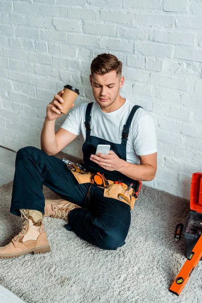 Instalador bonito usando smartphone enquanto segurando copo de papel — Fotografia de Stock