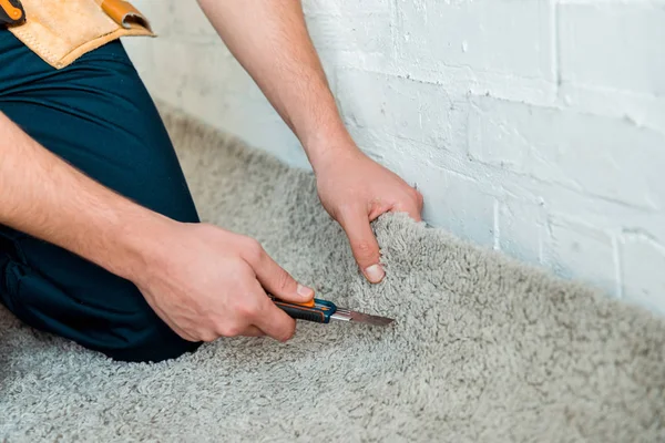 Vista ritagliato di installatore tenendo taglierina vicino tappeto — Foto stock