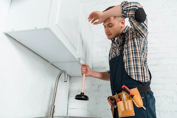 Installateur fatigué tenant le piston près du robinet dans la cuisine — Photo de stock