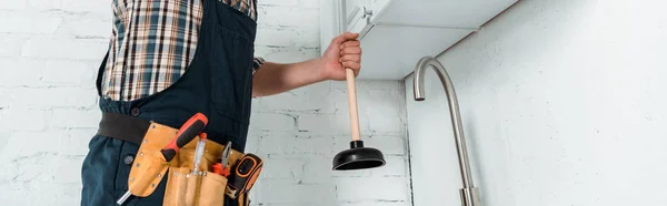 Tiro panorâmico do instalador segurando o êmbolo perto da torneira na cozinha — Fotografia de Stock