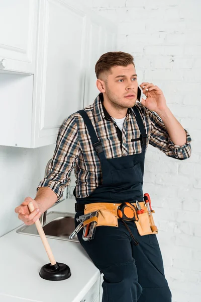 Instalador guapo hablando en el teléfono inteligente mientras sostiene el émbolo - foto de stock