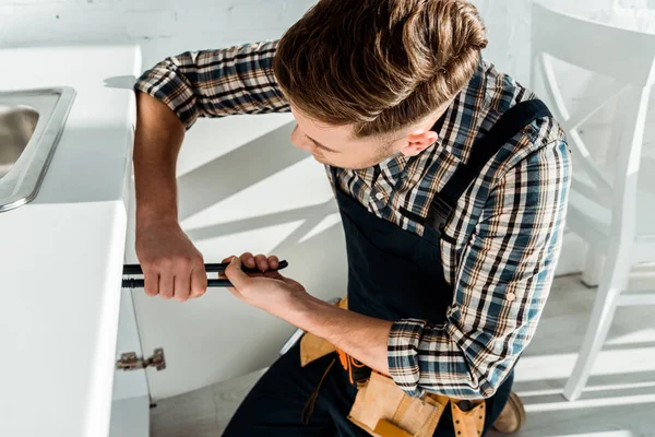 Installateur tenant des pinces à joint glissant tout en travaillant près de l'armoire de cuisine — Photo de stock