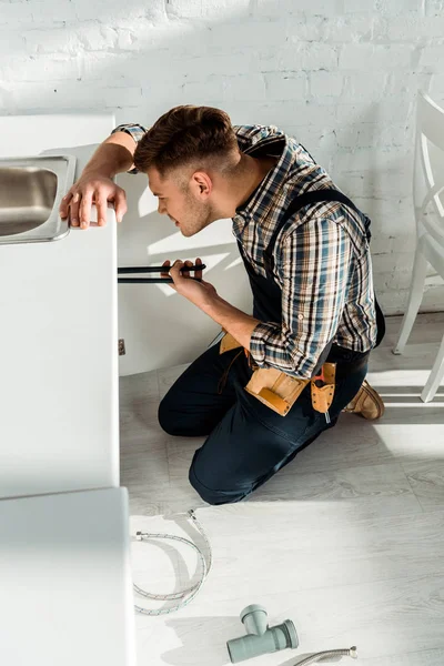 Seitenansicht des Installateurs, der eine Gleitfugenzange hält, während er in der Nähe von Küchenschränken arbeitet — Stockfoto
