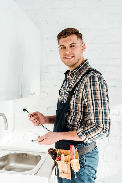 Fröhlicher Installateur hält Metallschlauch nahe Waschbecken — Stockfoto