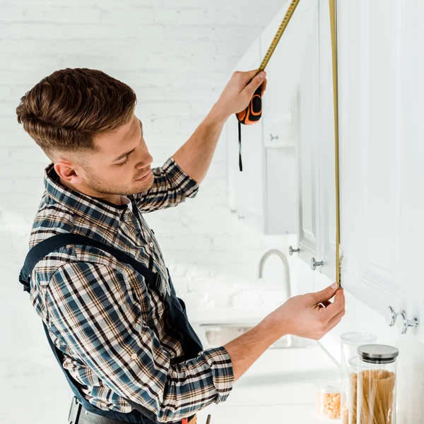 Handsome installer measuring white kitchen cabinet — Stock Photo