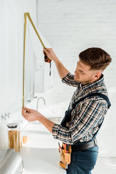 Instalador en overoles que miden gabinete de cocina blanco - foto de stock