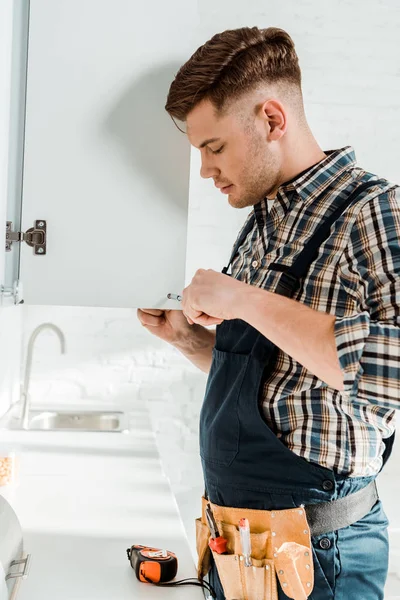 Profile of handsome installer holding screwdriver near kitchen cabinet — Stock Photo