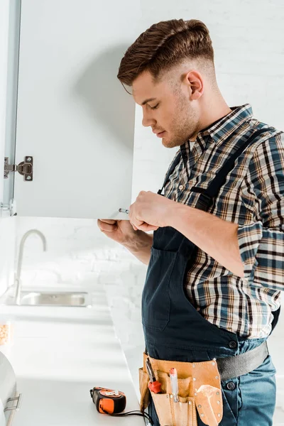 Perfil del instalador guapo que sostiene el destornillador cerca del gabinete de cocina — Stock Photo