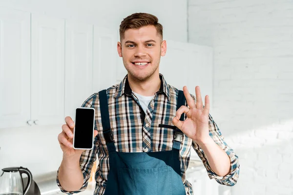 Happy installer holding smartphone with blank screen and showing ok sign — Stock Photo