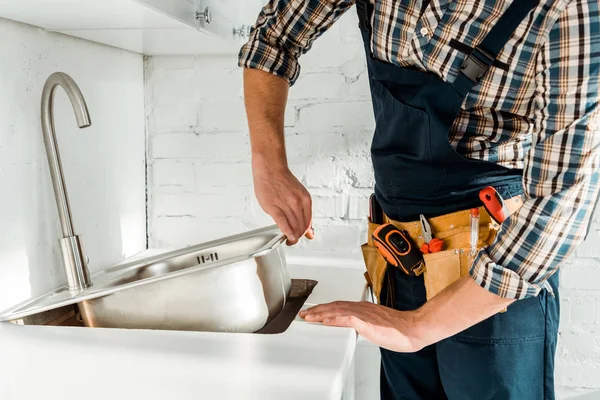 Vue recadrée de l'installateur tenant un évier métallique près du robinet dans la cuisine — Photo de stock