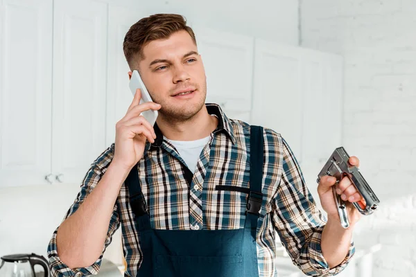 Gutaussehender Installateur hält Bauklammer während er mit dem Smartphone spricht — Stockfoto