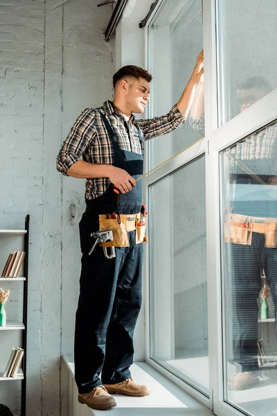 Installatore in piedi sul davanzale della finestra vicino alle finestre e tenendo il nastro di misurazione — Stock Photo