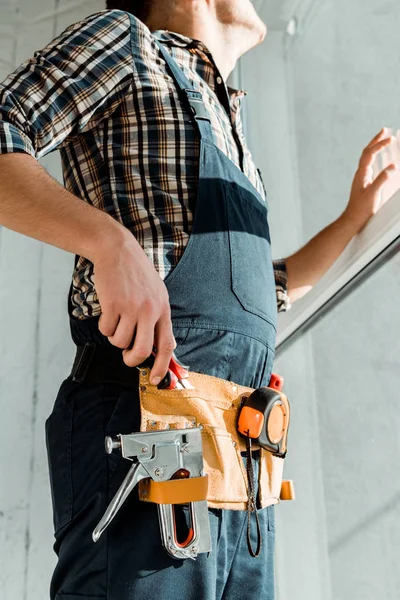 Ausgeschnittene Ansicht des Installateurs in Werkzeuggürtel und Overalls, der eine Zange nimmt — Stockfoto